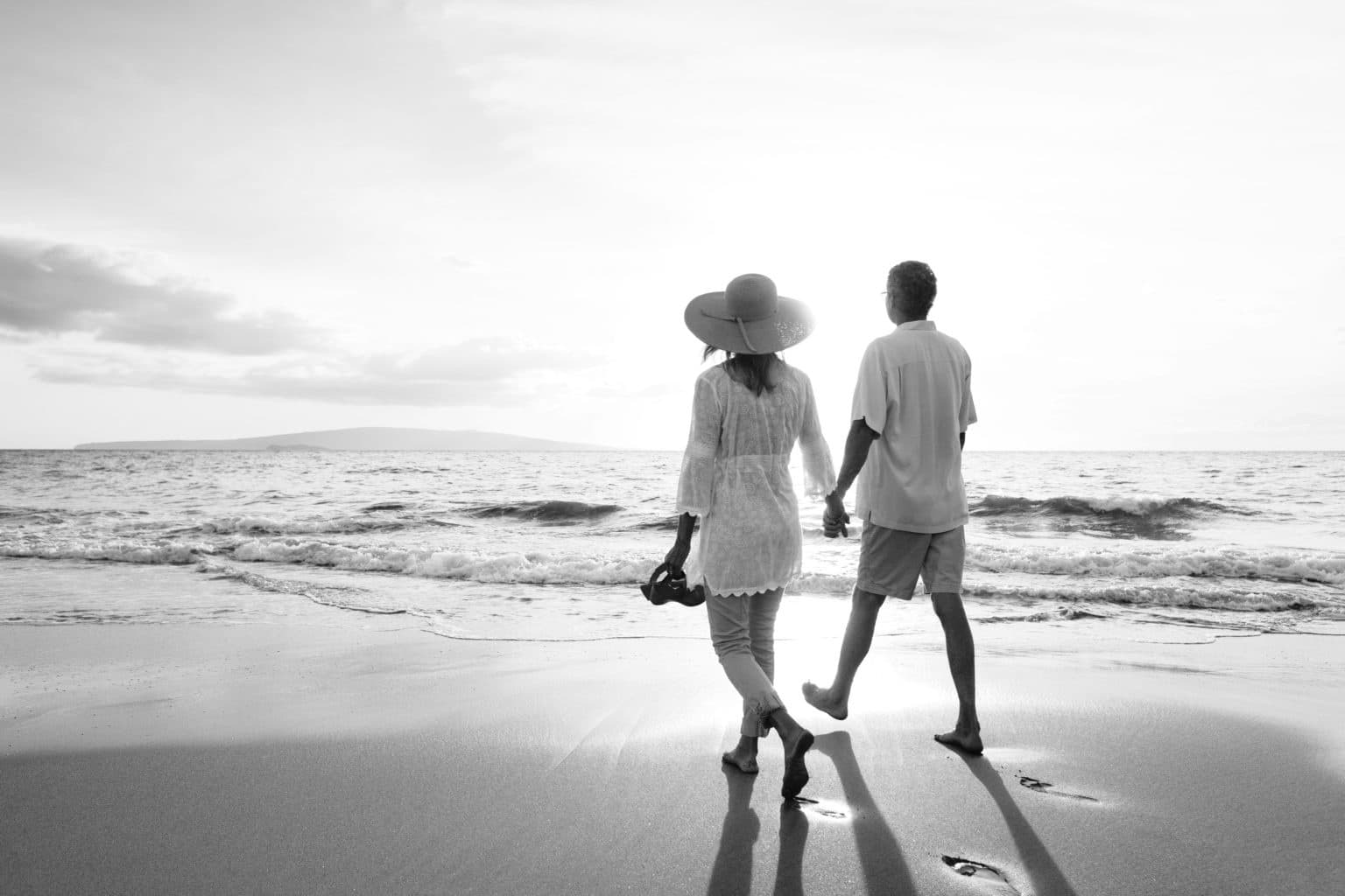 Intimkirurgi – Medelålderspar som håller hand njuter av en promenad på stranden vid solnedgång