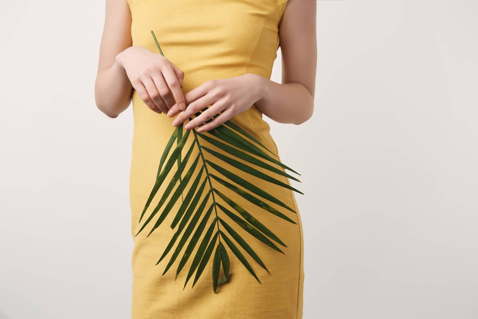 Kvinna i gul klänning hållandes ett grönt blad från en växt förbereder sig inför sin fettsugning av vensusberget