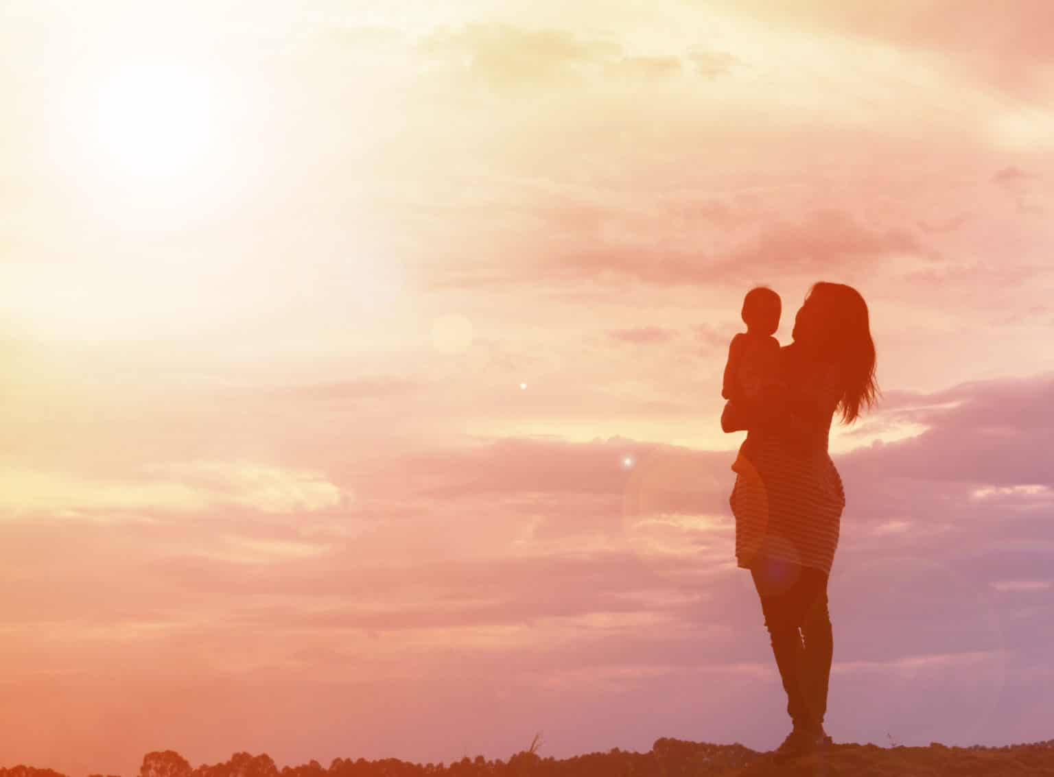 Siluett av en kvinna som håller sitt barn på en kulle vid en solnedgång